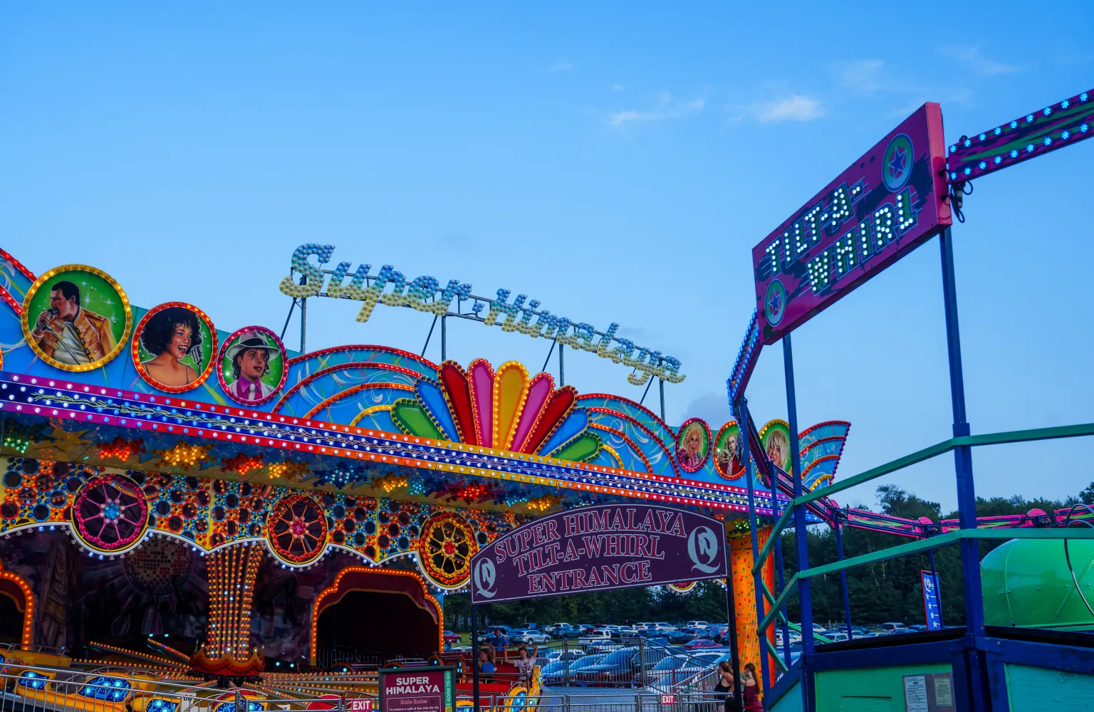 Landscape shot of Super Himalaya ride and Tilt a Whirl ride, lit up with colorful lights