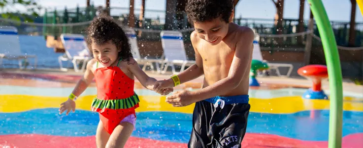 Two children holding hands and running through Splash Pad