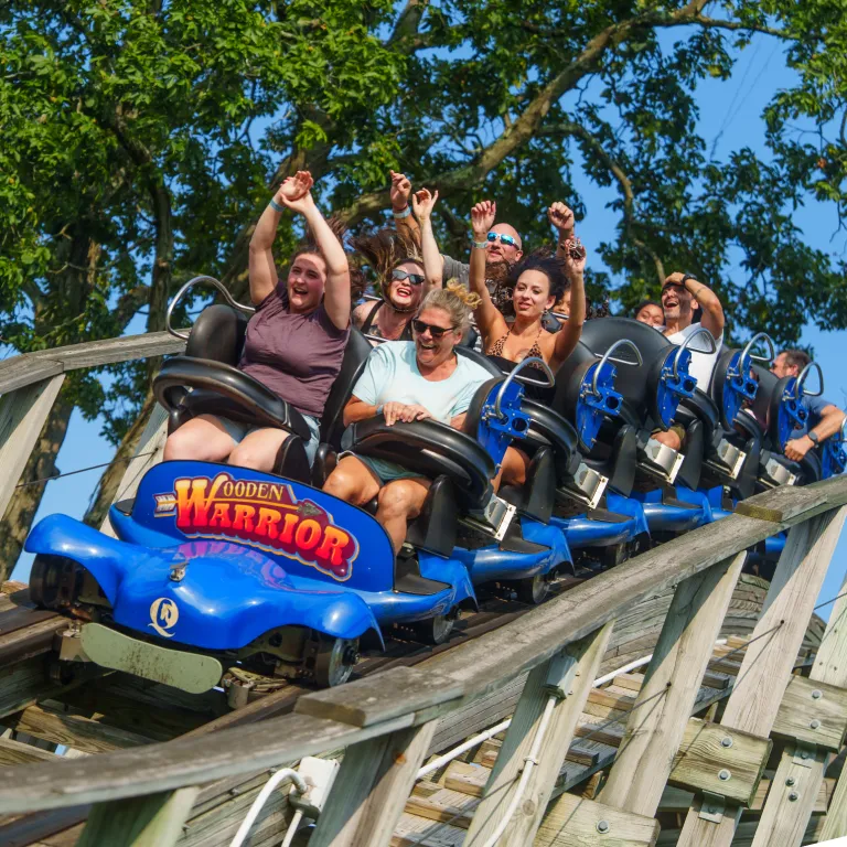 Group of people on Wooden Warrior roller coaster with arms up in air