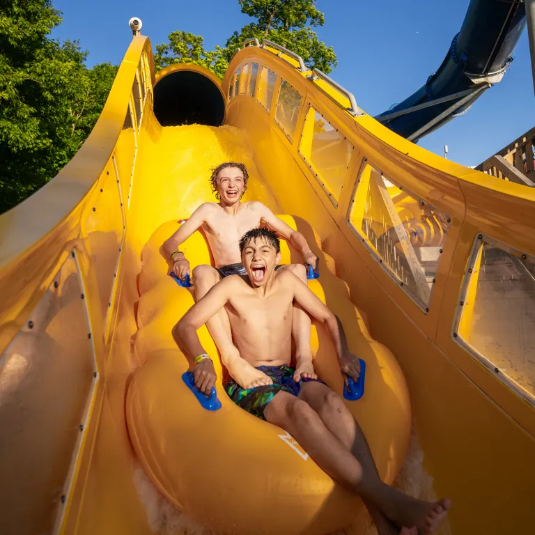 Two boys going down water slide in raft